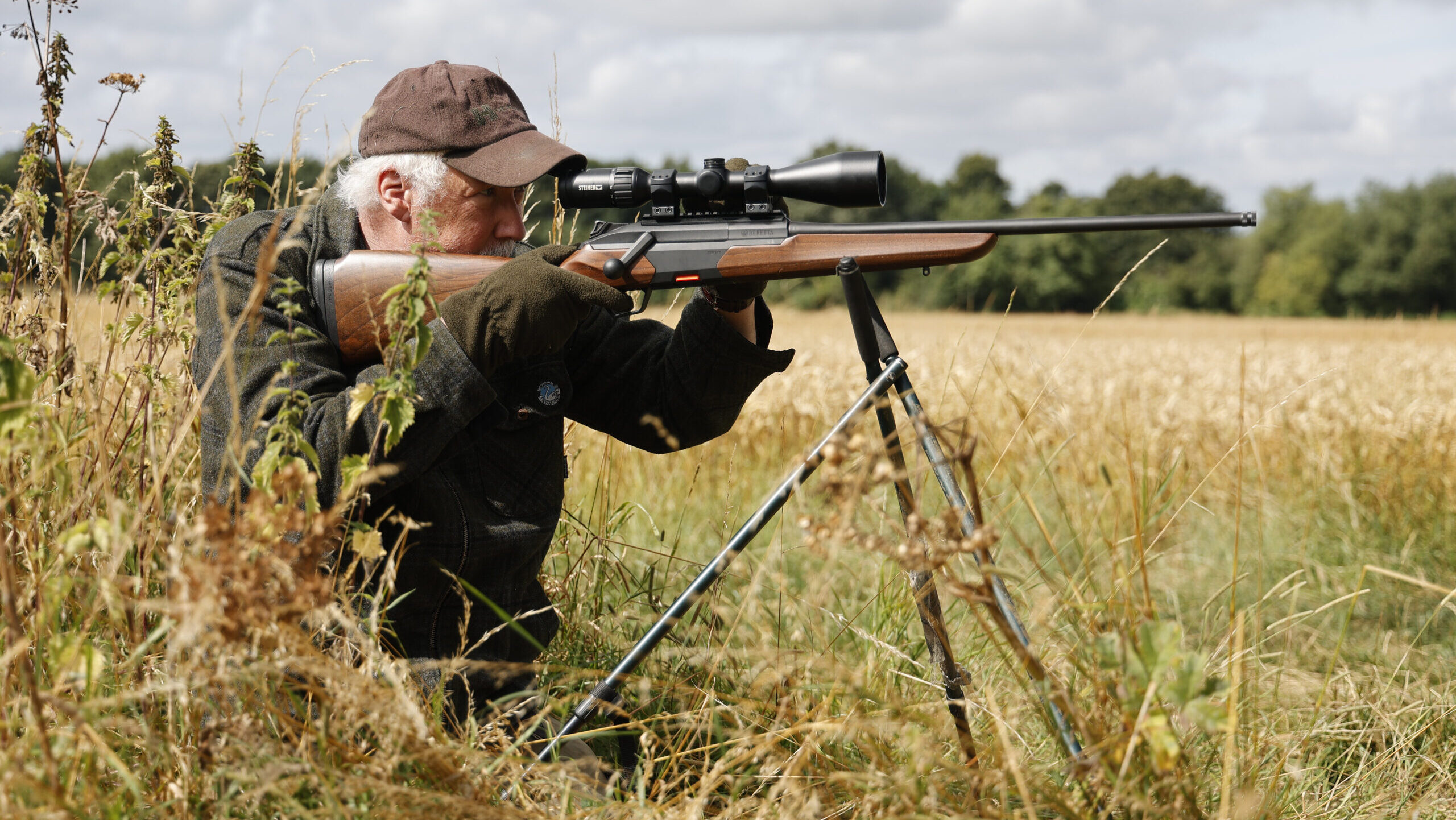 Man with a rifle on a tripod kneeling in long grass