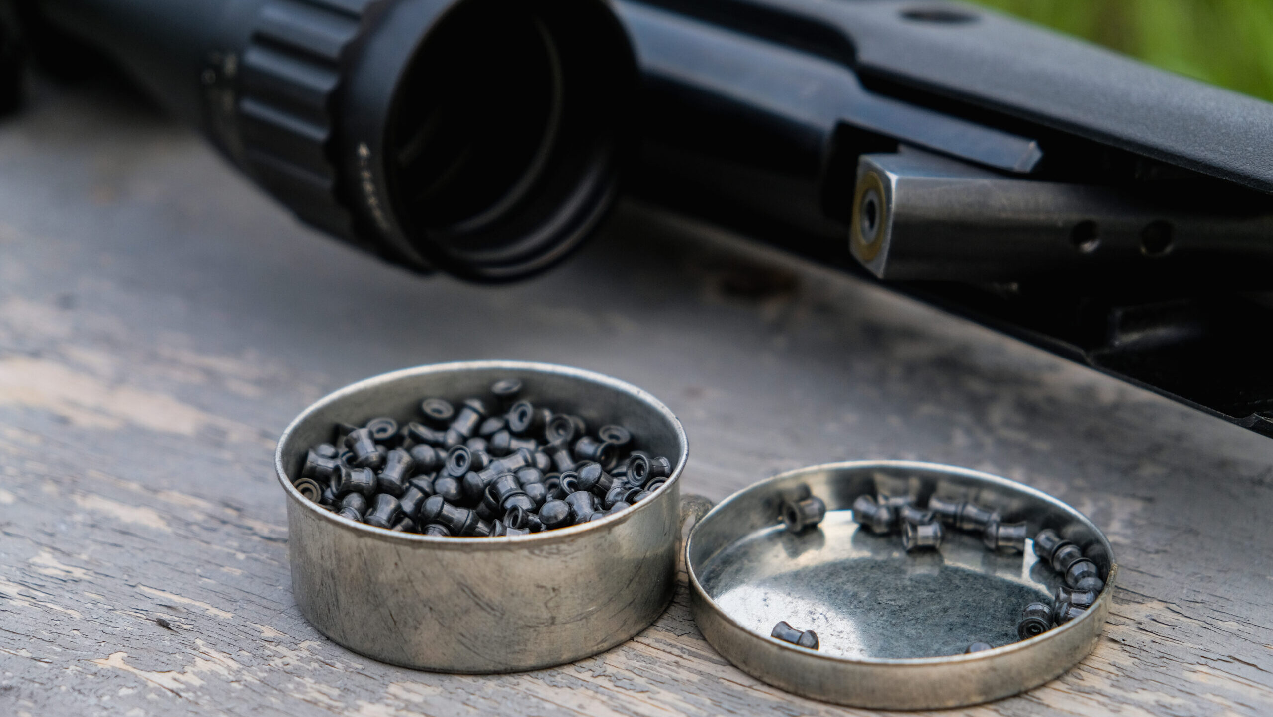 An open case of air rifle pellets next to an air rifle laying on a wooden bench